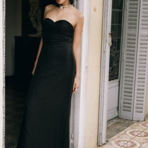A stylish woman in a black evening gown poses at a vintage doorway, exuding elegance.