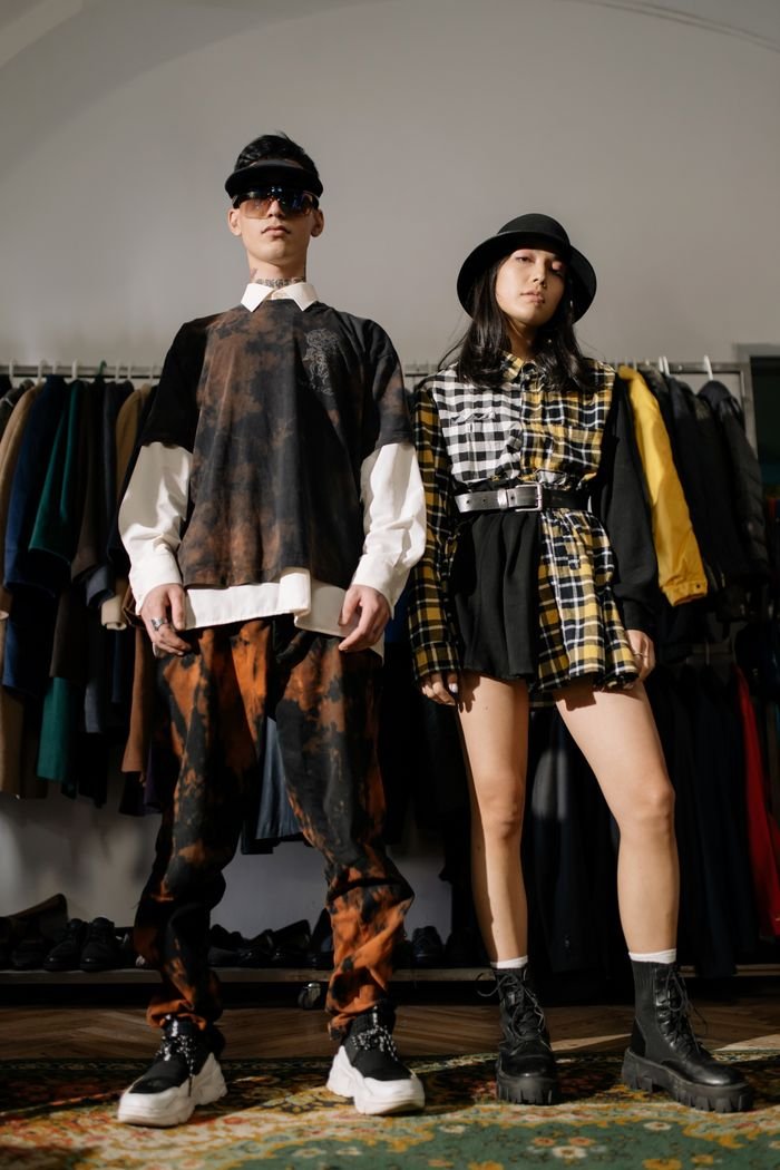 Home Two individuals pose confidently in a vintage clothing store showcasing urban fashion style.